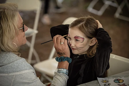 A little girl getting her face painted with a cat design at MerleFest